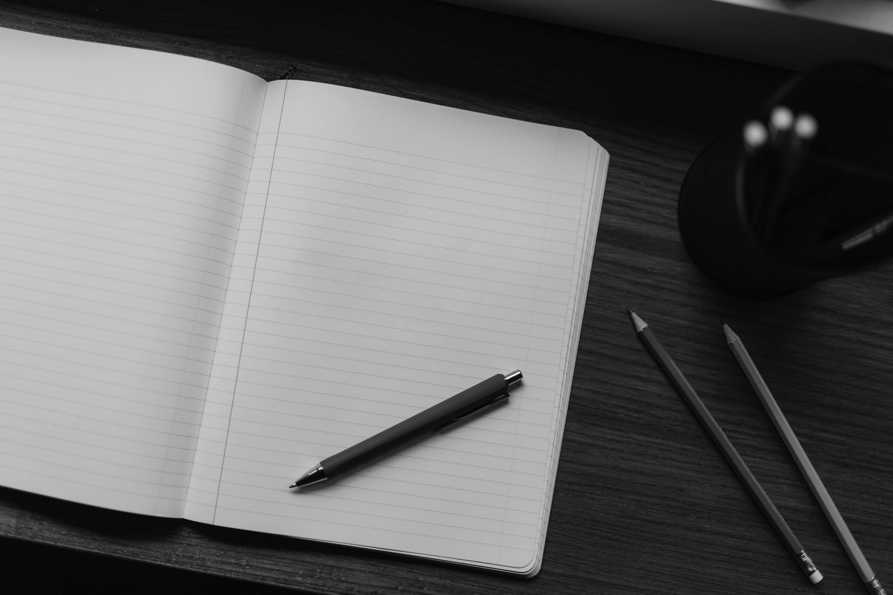 An open notebook with a pen and pencils on a desk